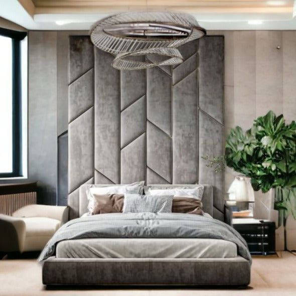 Modern bedroom with a large, textured gray headboard, an elegant gray bed, and a stylish ceiling light. A potted plant and cozy seating add warmth.